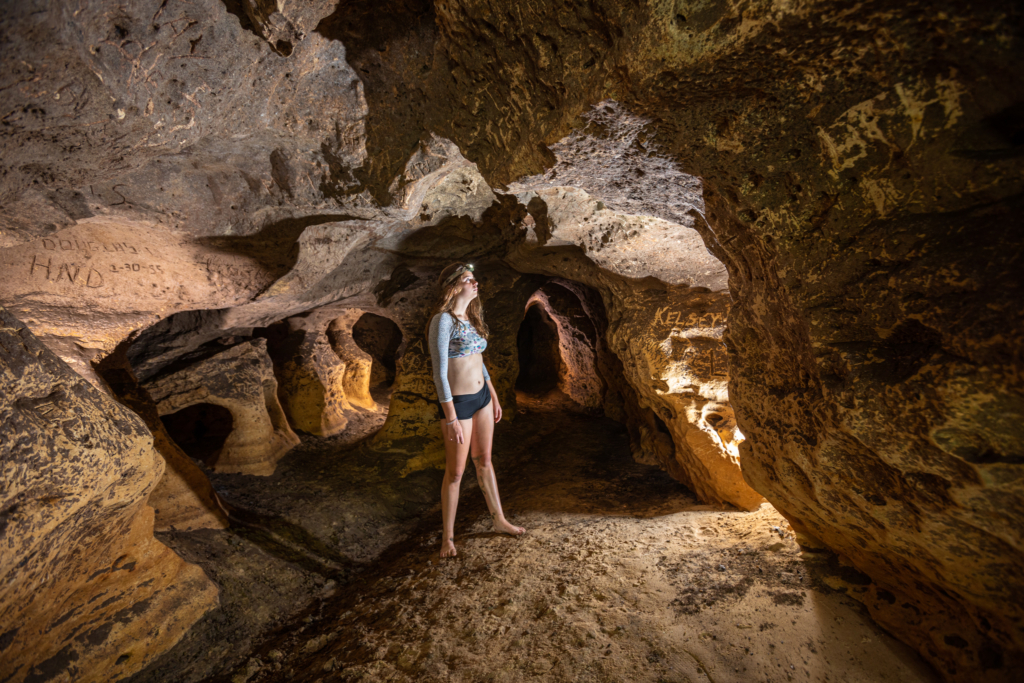 A girl with a headlamp stands in cave looking around