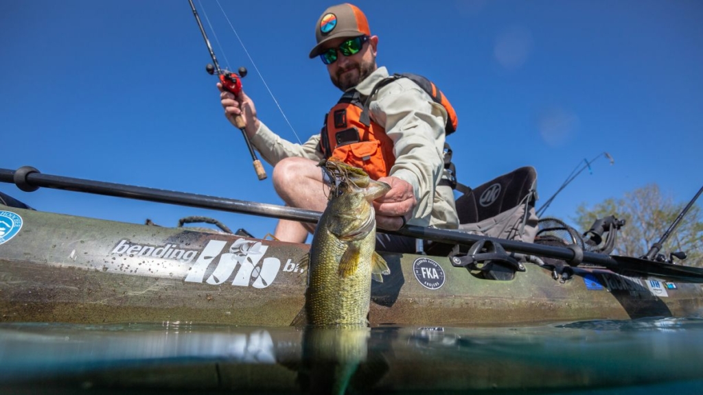 A man in a kayak holds a fish he just caught in the river